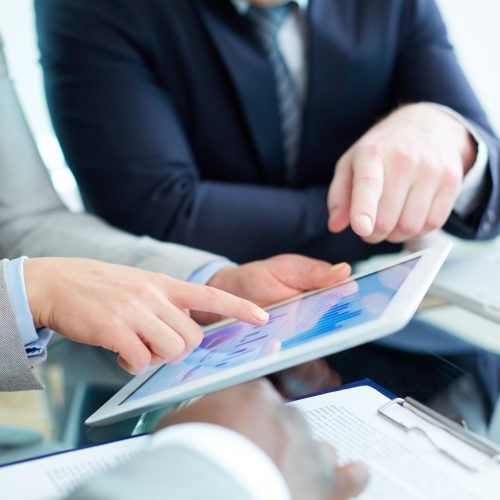 Image of human hands during discussion of business document in touchscreen at meeting