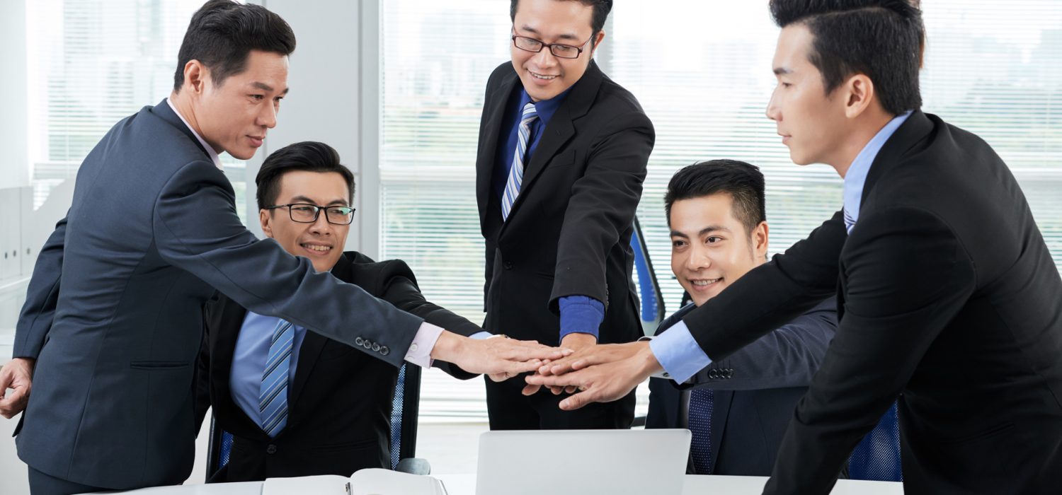 Ambitious team of white collar workers joining hands together while having productive working meeting at modern boardroom